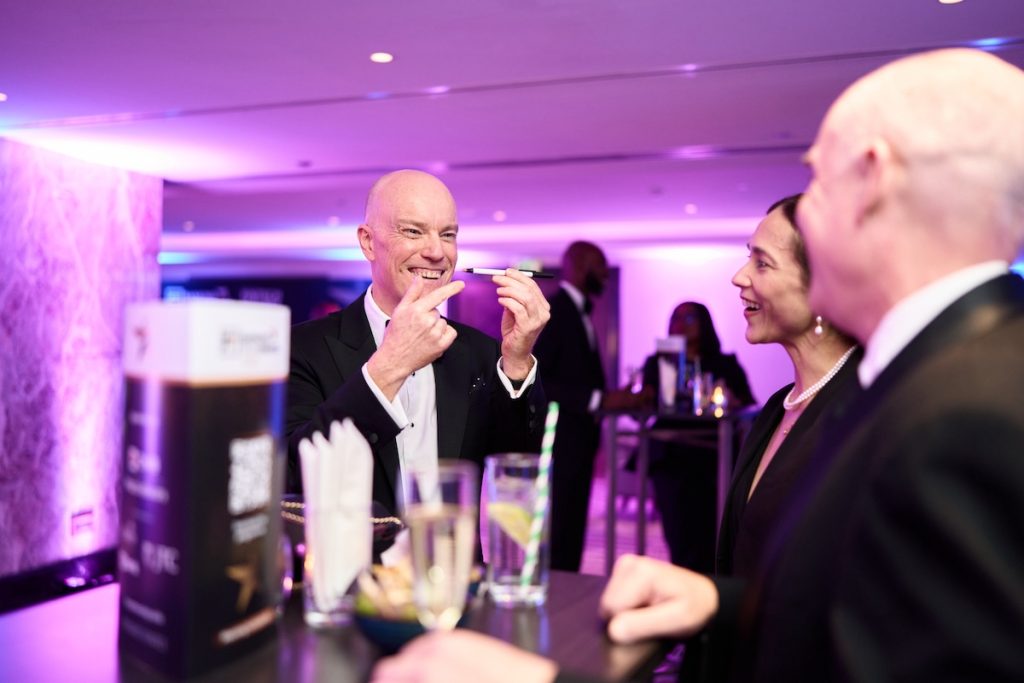 Darren Delaney in black tie performing a magic trick with a pen for guests at The Banking Tech Awards 2025